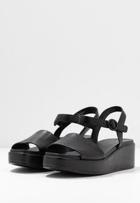 Sandali platform neri in pelle con punta aperta, cinturino alla caviglia regolabile e finitura liscia e opaca. Presentano un tacco chunky e un design minimalista.