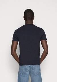 Camiseta de manga corta navy de tela de algodón, con un diseño de cuello redondo. La vista trasera muestra costuras mínimas y una textura suave. Se lleva con jeans de mezclilla azules.