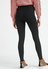 Zwarte legging met een gladde textuur, aansluitend ontwerp, gecombineerd met hoge sneakers met een panterprint. De trui heeft kabelgebreide mouwen.