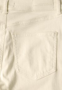 La tela de mezclilla blanca presenta un único bolsillo trasero con forma angular y costuras visibles. La cinturilla incluye una etiqueta de la marca.
