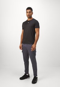 Zwarte t-shirt met korte mouwen heeft een klein wit logo. Grijze cargo broek heeft zijzakken en tappere benen. Zwarte sneakers maken de outfit compleet.