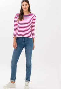 Haut à manches longues rayé en rose et blanc, associé à un jeans en denim bleu. Des baskets blanches complètent la tenue, offrant une coupe décontractée et des poignets retroussés.
