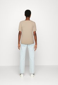 T-shirt beige a costine con maniche corte, abbinato a jeans dritti blu chiaro. La calzatura presenta sneakers bianche con accenti neri.