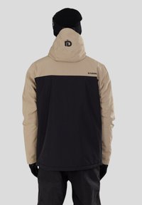 Dvoubarevná bunda v béžové a černé barvě, s kapucí, hladkým i texturovaným povrchem a logem na zadní straně. Jsou nasazeny černé rukavice.