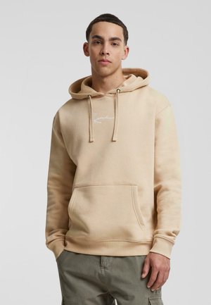 Sweatshirt beige à capuche avec une poche avant, des cordons de serrage et un subtle logo blanc sur la poitrine. Texture lisse, design décontracté.