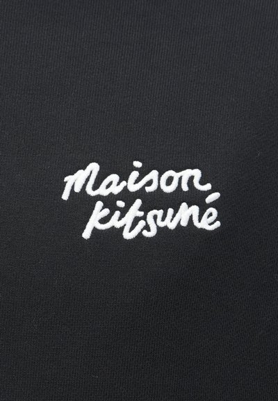 Čierna látka s ryhovanou textúrou, na ktorej je biele vyšívané písmo "Maison Kitsuné" v uvoľnenom písme.