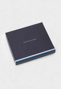 Cutie rectangulară de culoare albastru marin, cu dungi accent albii, roșii și albastre. Prezintă logo-ul "TOMMY HILFIGER" centrat pe partea de sus.