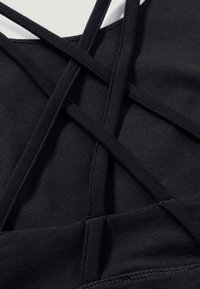 Black sports top featuring crisscross straps, made of stretchy fabric with a smooth texture. Clean seams and a fitted design.