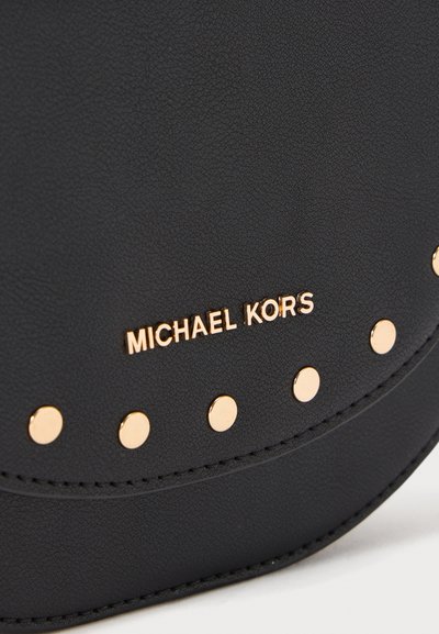 Svart texturerad syntetisk läderväska med guldfärgade detaljer och cirkulära nitar, med "MICHAEL KORS" präglat på framsidan.