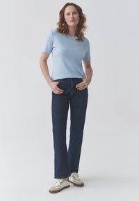 Haut bleu clair à manches courtes associé à un jean droit bleu foncé et des baskets beiges. Le haut est lisse, et le jean a une texture denim classique.