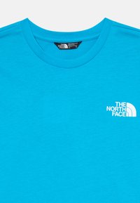 Világoskék kereknyakú póló, fehér "The North Face" logóval a bal mellen, és mérettag látható a garbón belül.