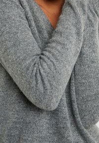 Pull en tricot gris à coupe ample et tissu texturé. Doté de manches longues avec des détails froncés et d'un décolleté en V profond.