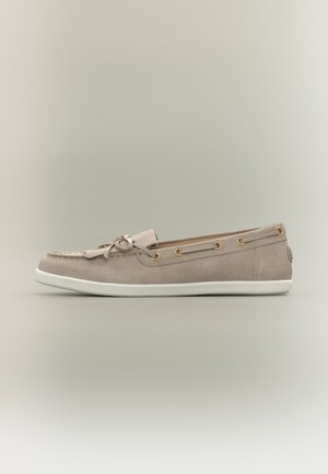 Μπεζ μοκασίνι από σουέτ με λευκή καουτσούκ σόλα, διακοσμητικό φιόγκο και χρυσά οπές στα πλάγια, εμφανίζεται σε αριστερή προφίλ όψη.