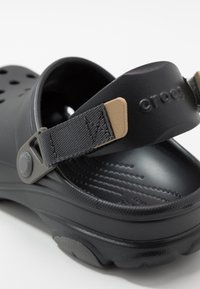 Sandales Crocs noires avec des trous de ventilation, une sangle texturée et une sangle de talon ajustable bicolore. Matériau léger avec une semelle intérieure à motifs.