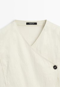 Cream-colored wrap blouse with a V-neck and a single black button on the right side, showing the brand label Massimo Dutti.