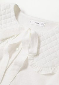 Blouse blanche avec col matelassé, bordure à volants, détail boutonné et noued en tissu au niveau de l'encolure, étiquette MNG taille S.