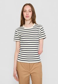 Stripet t-skjorte i krem og marineblå, korte ermer, rund halslinje og tettsittende design. Brukt med beige bukser.