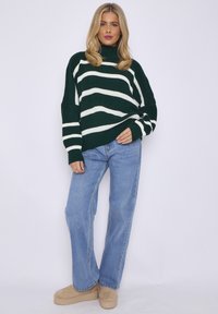 Green and white striped knit sweater with a turtleneck, paired with light blue wide-leg jeans and beige platform shoes.