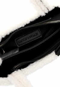 Intérieur noir d'un sac à main avec une doublure blanche, texturée et pelucheuse. Comprend une fermeture éclair et une étiquette en cuir avec "EMILY & NOAH" en relief.