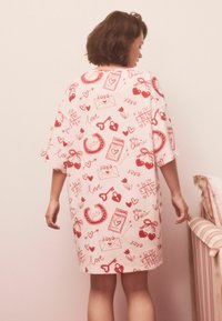Lyserød natkjole med røde grafikker af hjerter, nøgler og kuverter. Løs pasform, korte ærmer og knælængde design. Blød stoftekstur.