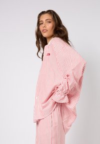 Koszula na guziki w paski z miękkiego materiału, z pionowymi różowo-białymi paskami. Luźny fason z podwiniętymi rękawami i małą metką z logo.