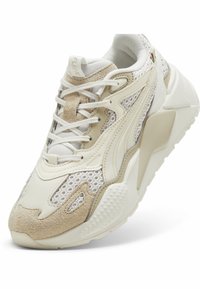 Zapato con una combinación de colores crema y beige, materiales de malla y gamuza, forma redondeada y un cuello acolchado con acentos texturizados.