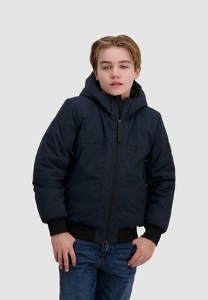 Marineblauwe pufferjack met een capuchon, vooraan met rits en ribbed cuffs, gedragen door iemand in denim jeans. De stof lijkt textuur te hebben en is geïsoleerd.