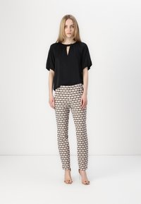 Black, short-sleeved top with a keyhole detail; loose fit. White pants with a geometric black and brown pattern. Beige, open-toed heels.