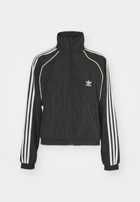 Svart sportjacka med hög krage, full dragkedja, vita ränder på ärmarna och en grön accent längs axlarna. Mjukt, lätt material.