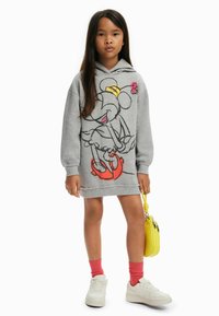 Vestido sudadera gris con un gran gráfico de Minnie Mouse, que lleva zapatos rojos y un bolso amarillo, complementado con calcetines rosas y zapatillas blancas.