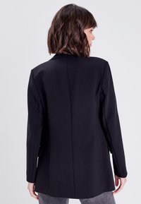 Black blazer with a tailored fit, structured shoulders, sharp lapels, and a single back vent. Smooth fabric and minimal detailing.