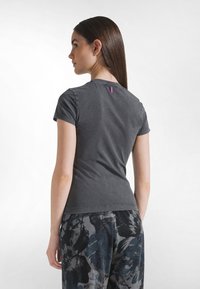 Grå bomulls-t-shirt med korta ärmar och rund halsringning. Har en liten lila varumärkestagg bakpå. Bärs med mönstrade byxor.