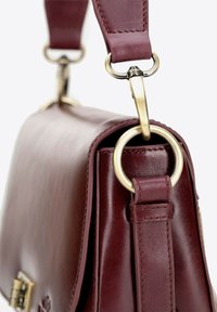Bordowa skórzana torebka o uporządkowanym kształcie, z wyraźnym złotym okuciem oraz odpinanym paskiem z metalowymi pierścieniami i detalami w postaci szwów.