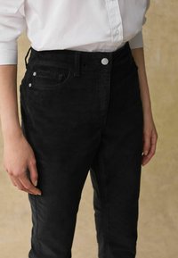 Pantalons en velours côtelé noir avec une coupe slim, dotés d'une fermeture à bouton sur le devant, d'accents en métal argenté et de poches latérales.