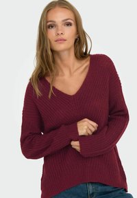 Maglione a maglia bordeaux con scollo a V, maniche lunghe e texture a coste; leggermente oversize con uno spacco laterale all'orlo.