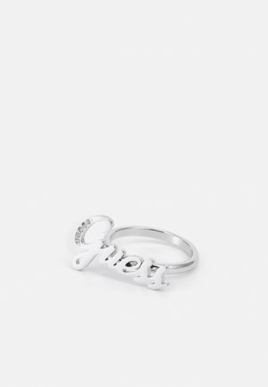 Zilveren ring met het woord "Guess" in cursief, met kleine ingelegde kristallen op de letter G, weergegeven op een witte achtergrond.