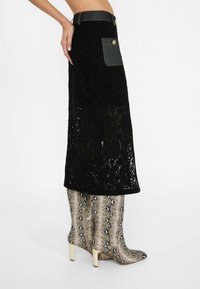 Jupe en dentelle noire avec des accents en denim et une poche, présentant une silhouette droite. Assortie à des bottes en cuir de serpent montantes avec une fermeture éclair.