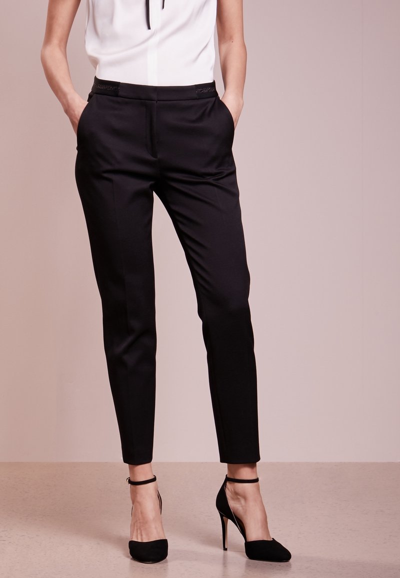 Pantalons habillés noirs avec poches et coupe slim, associés à des escarpins noirs à talons aiguilles, mettant en valeur une apparence élégante et soignée.