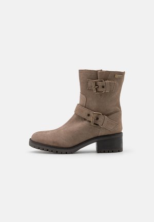 Bruine suède enkellaars met een vierkante neus, twee decoratieve gespen en een robuuste zwarte hak. Heeft een gestructureerd oppervlak en verstevigde stiksels.