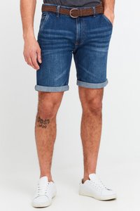 Mörkblå jeansshorts med uppvikt nederkant, fem fickor och ett flätat brunt bälte. Kombination med vita sneakers. Tatuering synlig på benet.