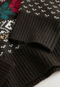 Pruunista kootud kampsunist, millel on soonikkoes varrukad, geomeetriline muster valge, punase ja rohelise värviga ning pehme tekstuur.