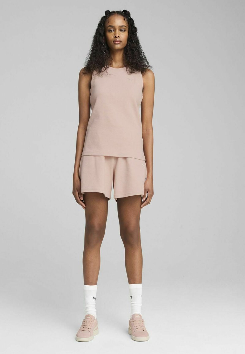 Top senza maniche rosa e pantaloni corti abbinati in tessuto texturizzato, abbinati a sneakers rosa chiaro e calzini bianchi con logo nero.
