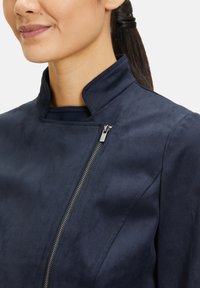 Marinblå jacka med hög krage och siddragkedja. Mjuk, mockaliknande textur med minimalistisk design. Inga synliga mönster eller accenter.