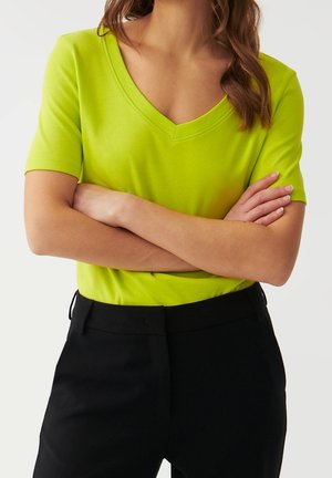 Limoengroene V-hals T-shirt met korte mouwen en een zachte textuur, gecombineerd met een zwarte broek. Het shirt heeft een aansluitende pasvorm en een casual ontwerp.