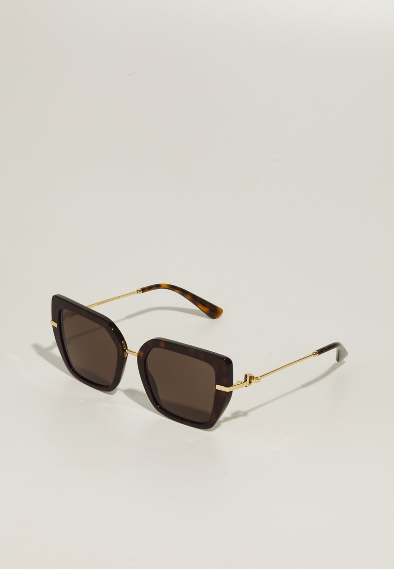 Kvadratne tamno smeđe sunčane naočale s tankim zlatnim metalnim krakovima i vrhovima od kornjačine oklopke položene na svijetlu površinu.