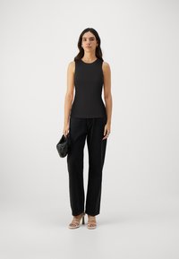 Svart ermeløs topp med ribbestruktur, sammen med brede svarte jeanstbukser. Modellen holder en liten svart veske og bruker beige stroppestøveletter.