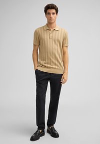 Beige geribbelde polo met kraag, drie knopen en korte mouwen, gecombineerd met donkere broeken en zwarte loafers. Schone ontwerp en textuur.