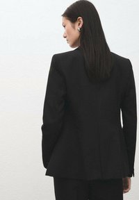 Czarna, dopasowana marynarka z usztywnionymi ramionami i lekko rozszerzającym się krojem. Gładka tkanina, bez widocznych wzorów, minimalizm w designie.