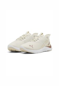 Zapatillas deportivas beige con una parte superior de tejido texturizado, suela blanca y un discreto detalle de logo en rosa. Presenta acentos en dos tonos en el talón.