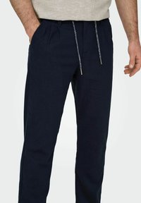 Pantaloni blu navy realizzati in tessuto morbido, dotati di un cordoncino con punte in metallo, tasche laterali e un design dalla vestibilità rilassata.